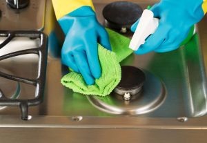 29603974 - closeup horizontal image of hands wearing rubber gloves while cleaning stove top range with spray bottle and microfiber rag